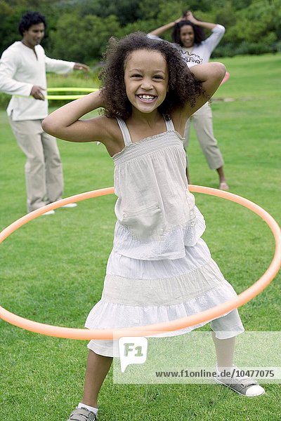 MODELL FREIGEGEBEN. Mädchen spielt mit einem Hula-Hoop-Reifen mit ihrer Familie in einem Garten Mädchen spielt mit einem Hula-Hoop-Reifen