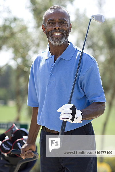 MODEL RELEASED. Golf player. Man holding a golf club and pulling his golf bag on a trolley. Golf player