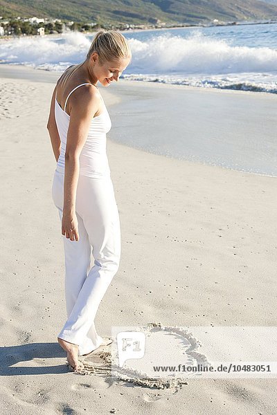 MODEL RELEASED. Heart in the sand. Woman drawing a heart-shape on a sandy beach. Heart in the sand