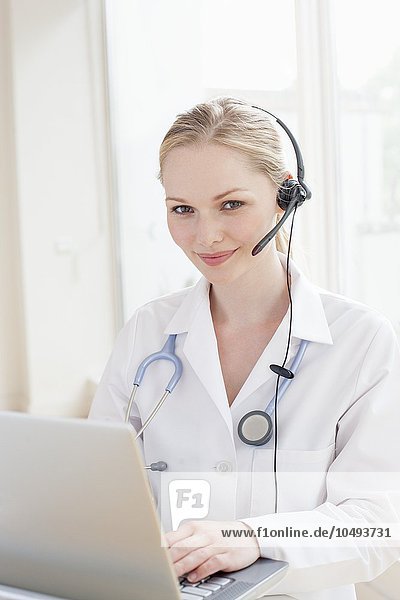 MODEL RELEASED. Doctor using a laptop computer and headset. Doctor using a laptop computer