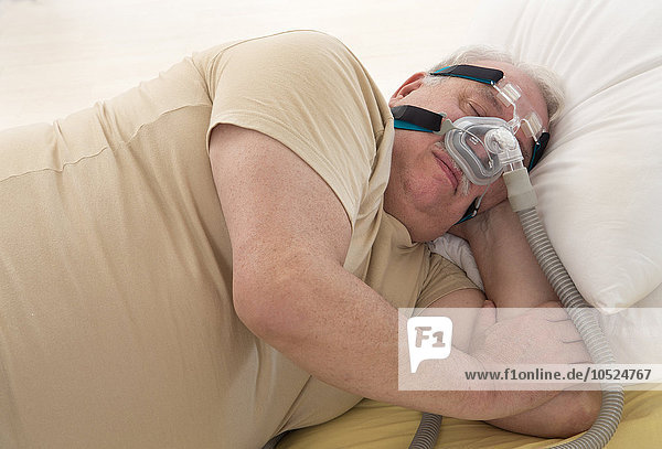 Übergewichtiger Mann  der eine CPAP-Maske (Continuous Positive Airway Pressure) zur Behandlung des Schlafapnoe-Syndroms verwendet.