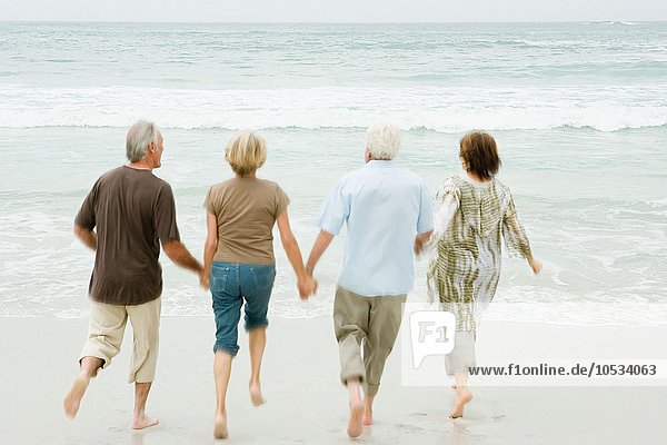 Vier ältere Erwachsene  die ins Meer rennen.