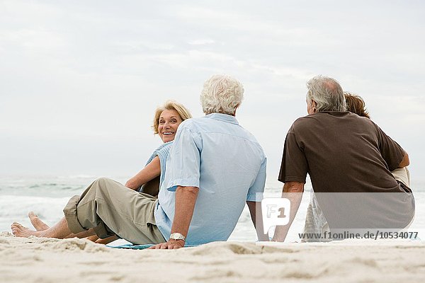 Vier ältere Erwachsene sitzen am Strand.