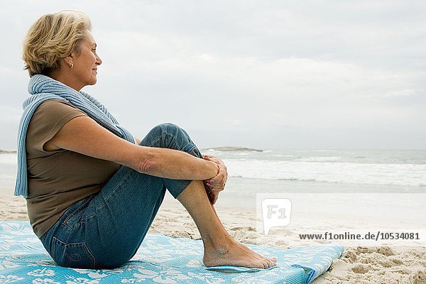 Ältere erwachsene Frau saß am Strand.