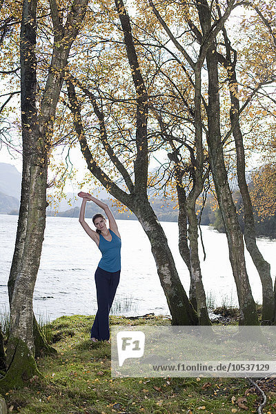 Frau praktiziert Yogastellung unter Bäumen
