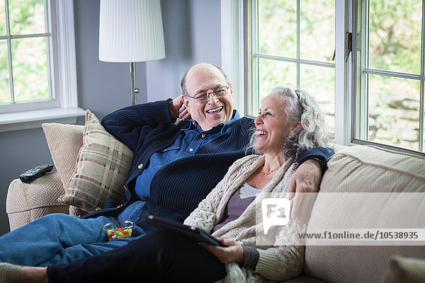 Senior couple using digital laptop on sofa at home
