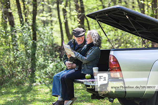 Seniorenpaar beim Lesen der Karte auf dem Kofferraum im Wald