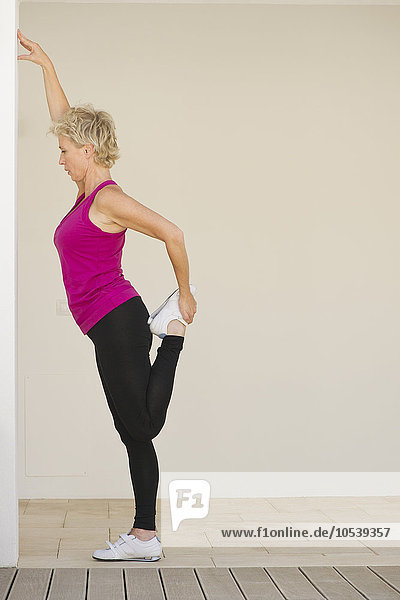 Mature woman stretching against wall  side view