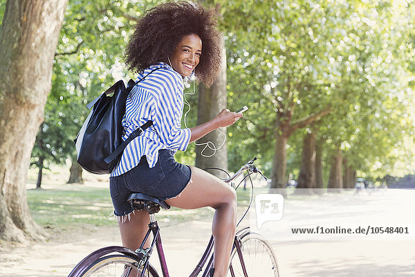 Portrait lächelnde Frau auf dem Fahrrad mit mp3-Player und Kopfhörer im Park