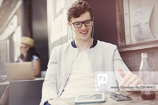 Lächelnder junger Mann hört Musik mit Kopfhörern und mp3-Player auf dem Bürgersteig Cafe