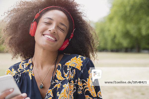 Begeisterte Frau beim Musikhören mit Kopfhörer und mp3-Player im Park