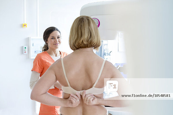 Nurse helping patient prepare for mammogram in examination room