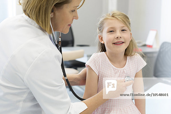 Pediatrician using stethoscope on girl patient in examination room