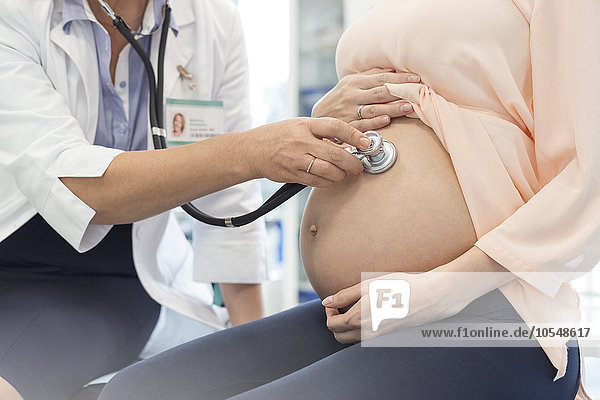 Doctor using stethoscope on pregnant patient’s stomach