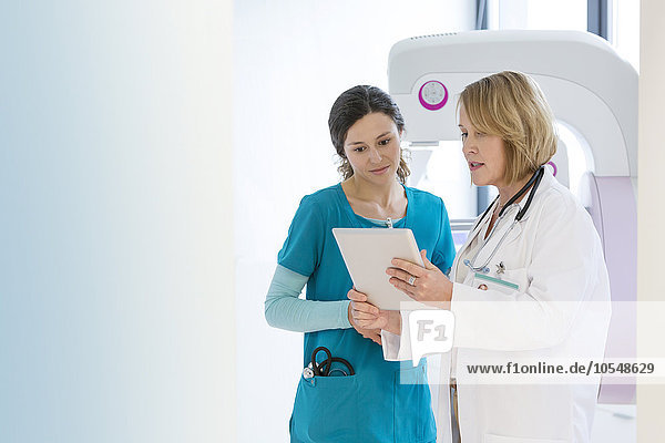 Arzt und Krankenschwester mit digitalem Tablett im Untersuchungsraum