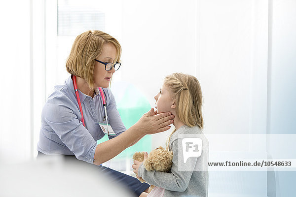 Pediatrician checking girl patient’s glands in examination room