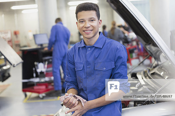 Porträt eines lächelnden Mechanikers  der sich in der Autowerkstatt auf das Auto stützt.