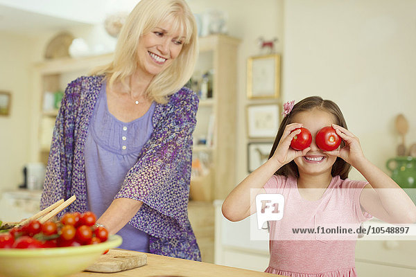 Portrait verspielte Enkelin  die in der Küche die Augen mit Tomaten bedeckt