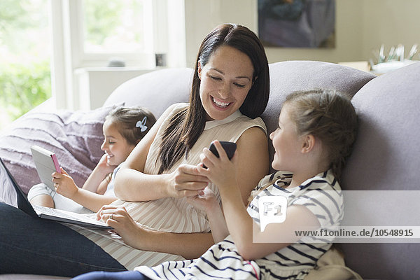 Mutter und Töchter mit Handy  Laptop und digitalem Tablett auf Sofa