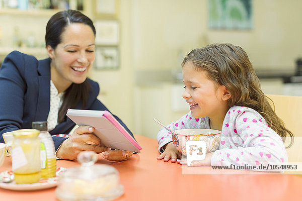 Mutter und Tochter mit digitalem Tablett am Frühstückstisch
