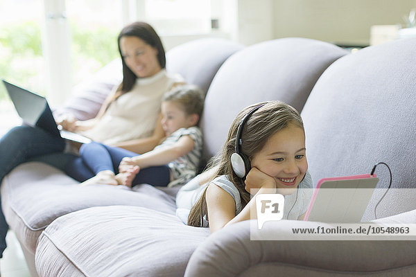 Mädchen mit Kopfhörer und digitalem Tablett auf dem Wohnzimmersofa
