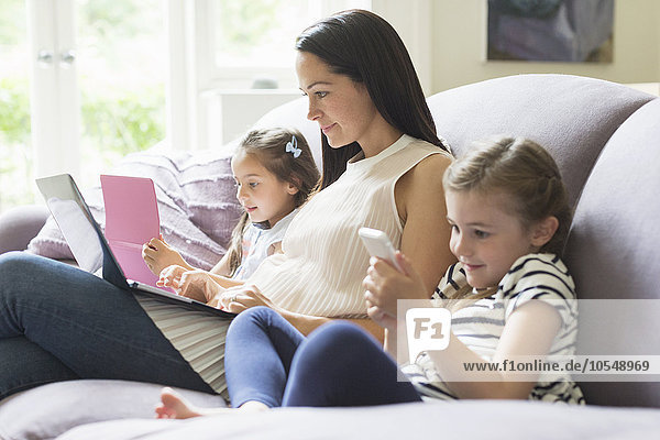 Mutter und Töchter mit Laptop  Handy und digitalem Tablett auf Sofa