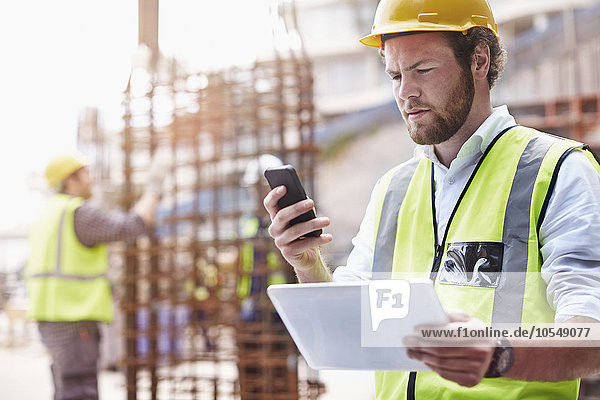 Bauarbeiter mit digitalem Tabletttext mit Handy auf der Baustelle