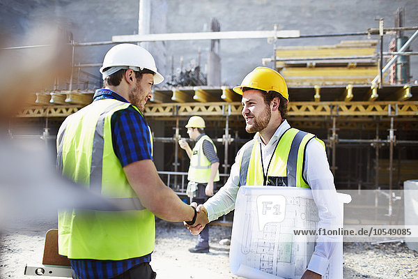 Construction worker and engineer with blueprints handshaking at construction site