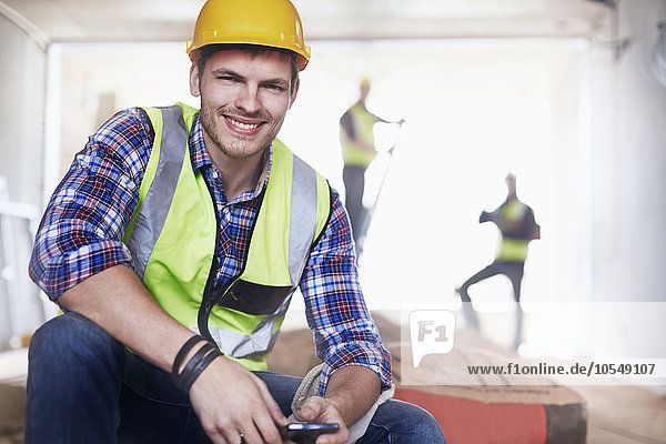 Portrait lächelnder Bauarbeiter mit Handy auf der Baustelle