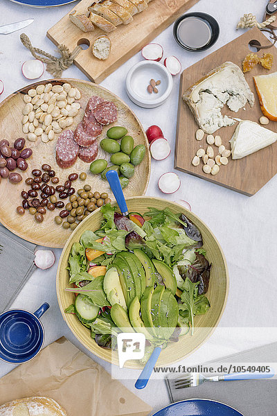 Schrägansicht auf eine Käseplatte  Käse  Oliven  Nüsse und eine Schüssel Salat auf einem Tisch.