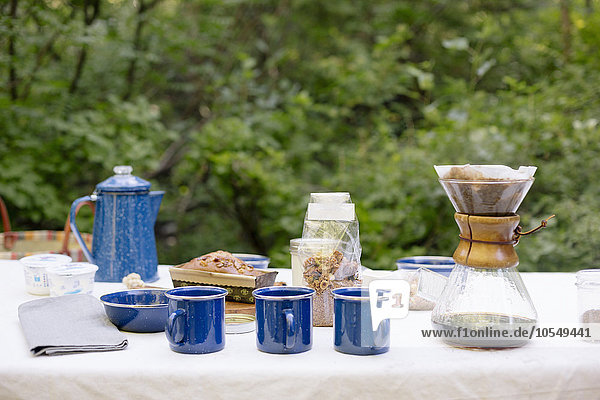 Tisch in einem Garten  mit Kaffeemaschine  Tassen und Schalen  einem Kuchen und Müsli.
