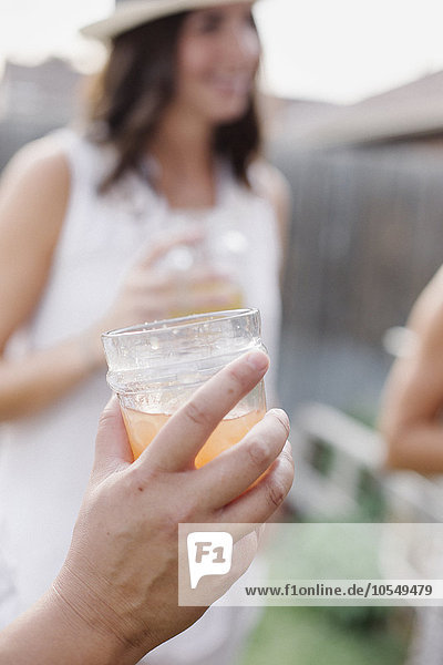 Nahaufnahme einer Hand  die ein Getränk hält  im Hintergrund eine Frau.