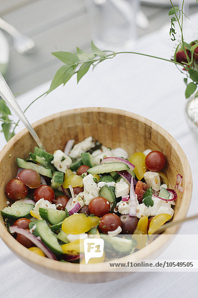 Eine Schüssel Salat auf einem Tisch in einem Garten mit frischen Tomaten  Gurken und Paprika.