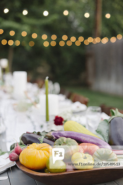 Langer  mit Tellern und Gläsern gedeckter Tisch  Essen und Trinken in einem Garten  im Vordergrund eine Schale mit Gemüse.