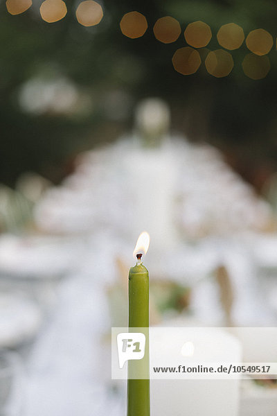 Eine brennende Kerze auf einem mit Tellern und Gläsern gedeckten Tisch  Essen und Trinken in einem Garten.