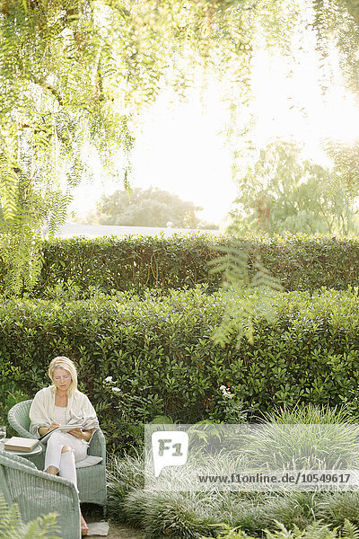 Blonde Frau sitzt in einem Korbstuhl in einem Garten.