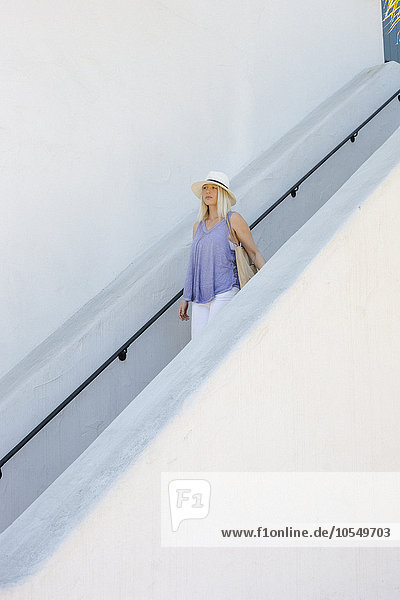 Blonde Frau mit Hut  die eine Treppe hinuntergeht.