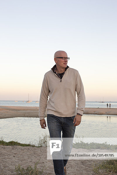 Bald man walking on a sandy beach by the ocean.