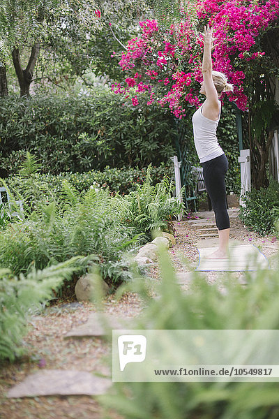 Blonde Frau beim Yoga in einem Garten.