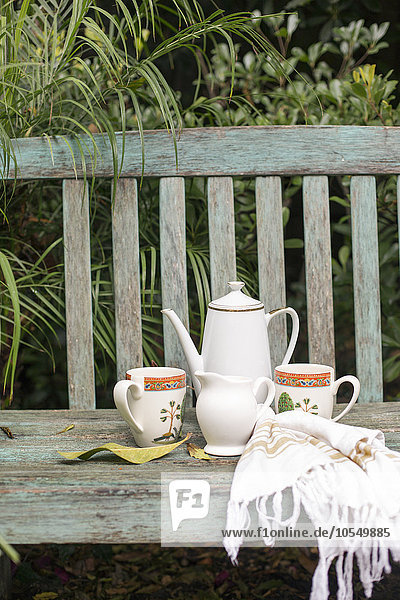 Kaffeekanne und Tassen auf einer hölzernen Gartenbank.