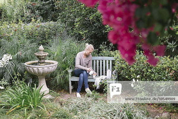 Frau sitzt auf einer Holzbank in einem Garten und macht eine Pause.