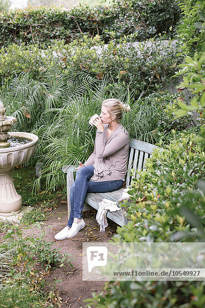 Frau sitzt auf einer Holzbank in einem Garten und macht eine Pause.