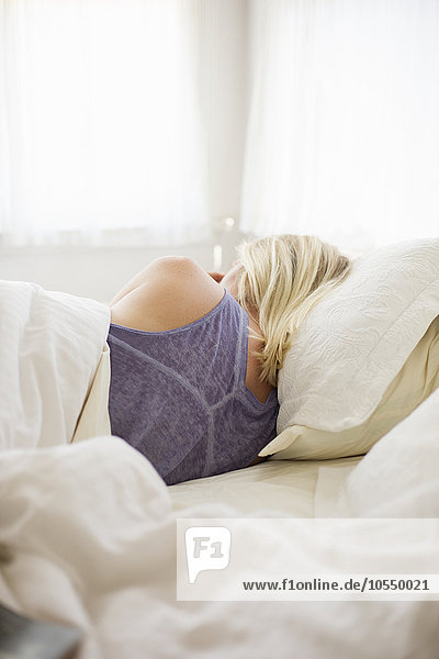 Blonde Frau schläft in einem Bett mit weißer Bettwäsche.