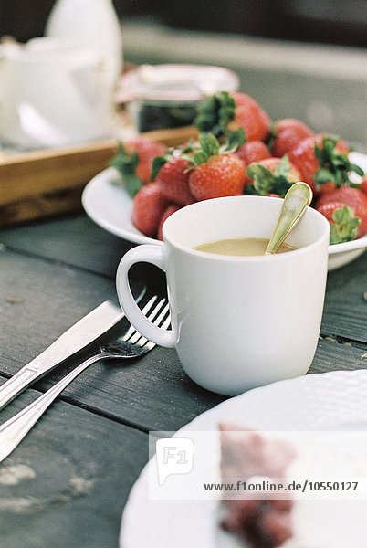 Eine Tasse Tee und ein Teller mit frischen Erdbeeren auf einem Tisch.