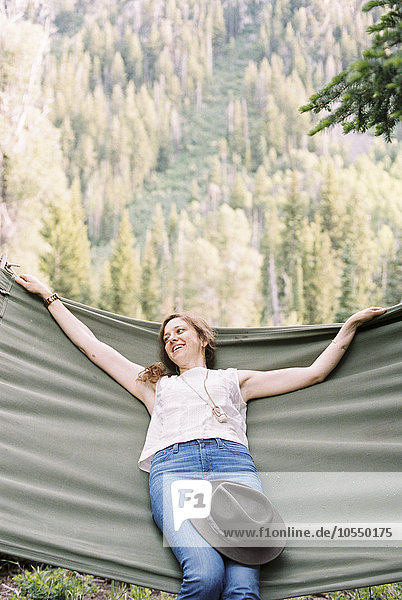 Woman relaxing in a large hammock in a forest.