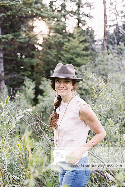 Lächelnde Frau mit Hut  die in einem Wald steht.