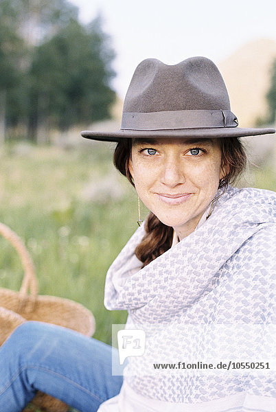 Eine Frau mit Hut und Wolltuch sitzt auf einer Wiese.