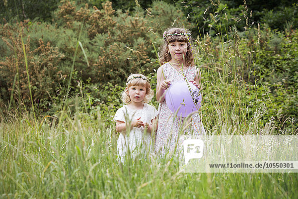 Two young girls standing in a meadow.
