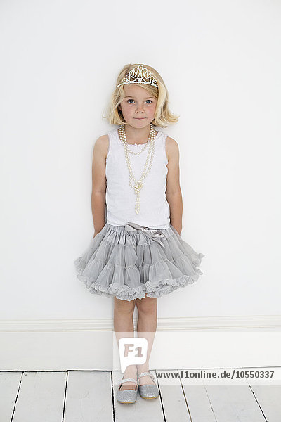 Junges Mädchen,  das ein Diadem und eine Perlenkette trägt und für ein Bild in einem Fotostudio posiert.