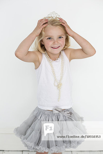 Junges Mädchen  das ein Diadem und eine Perlenkette trägt und für ein Bild in einem Fotostudio posiert.